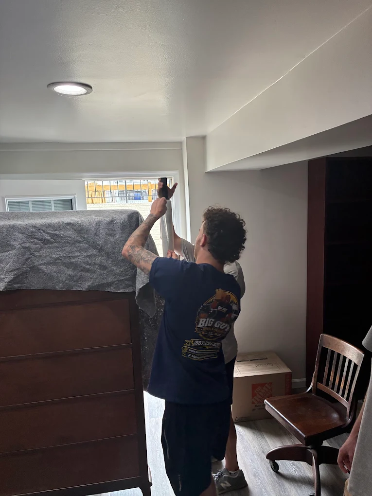 Two movers wrapping a tall dresser