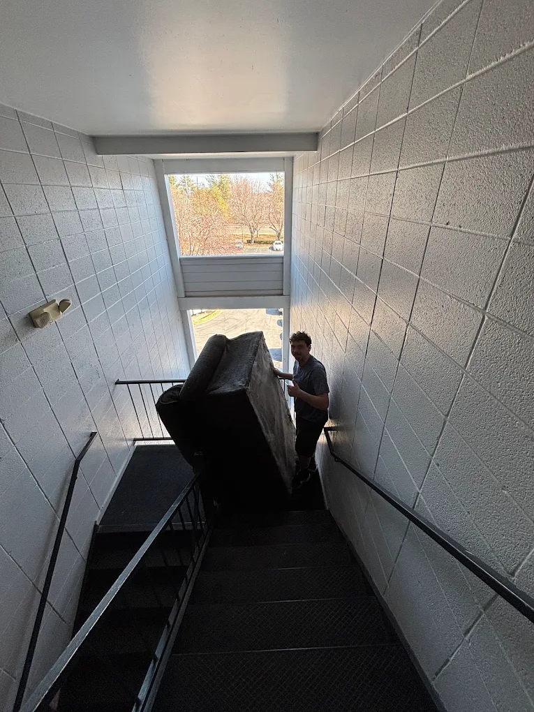Crew guiding a wrapped couch down an apartment stairwell