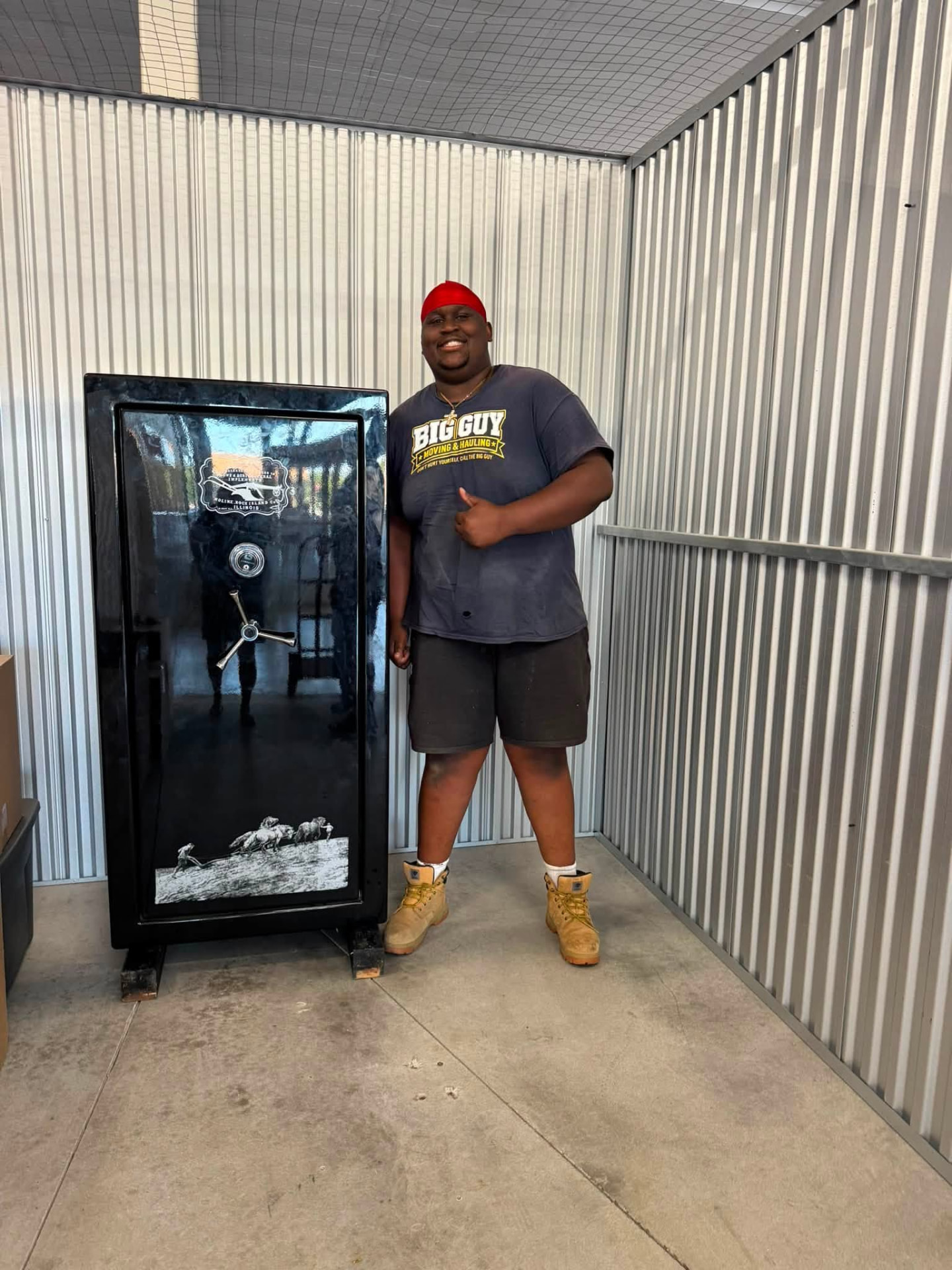 Aaron in a Big Guy Moving shirt beside a black gun safe inside a storage unit