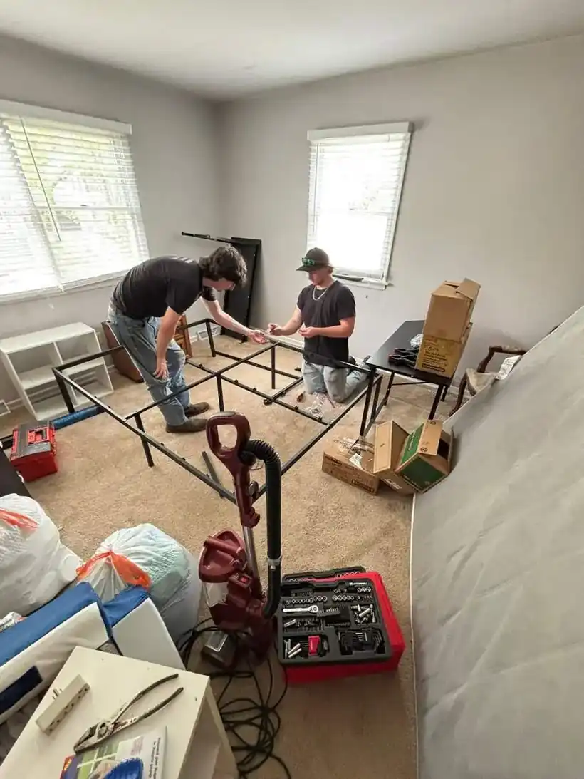 Big Guy Moving crew assembling a metal bed frame in a bedroom