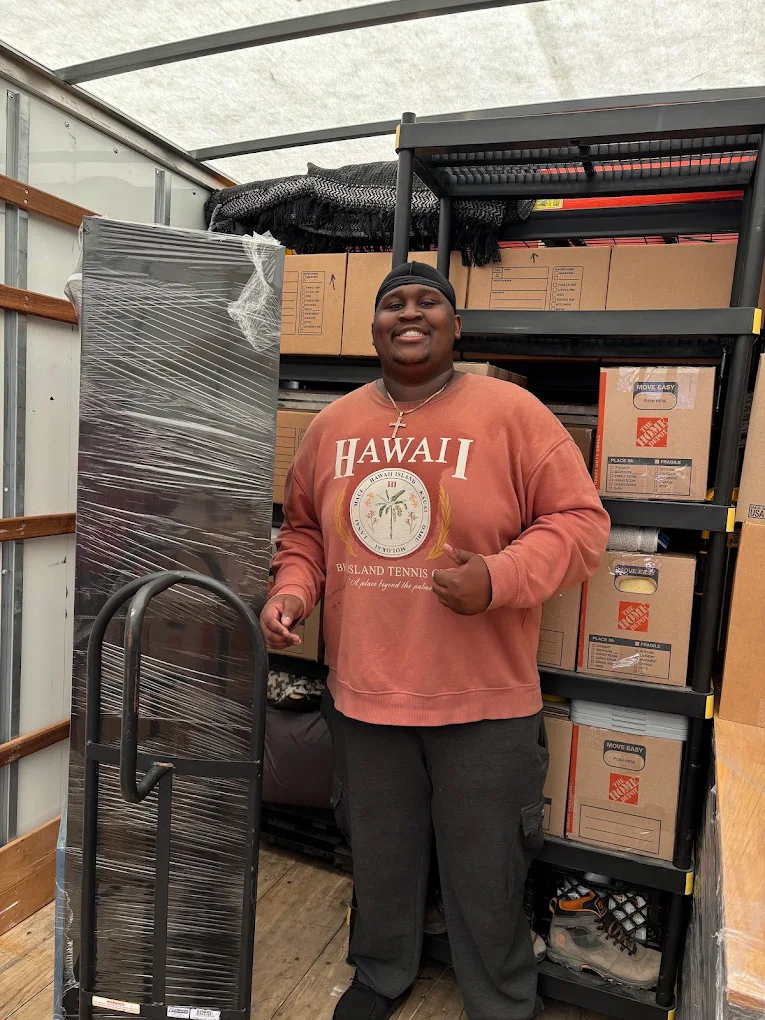 Aaron smiling inside a packed moving truck with shelving and boxes