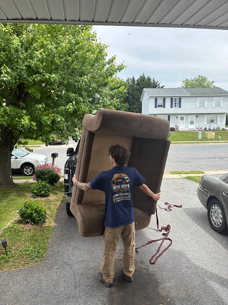 Mover in a Big Guy Moving tee lifting a recliner sofa into a truck