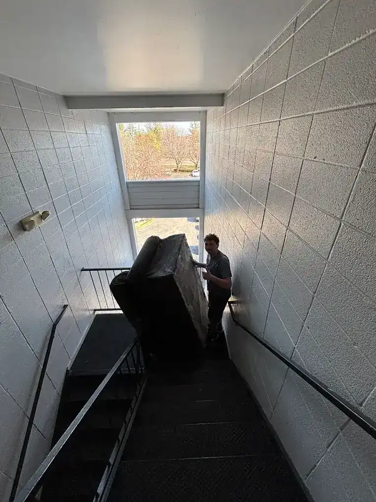 Crew member guiding a wrapped couch down an apartment stairwell
