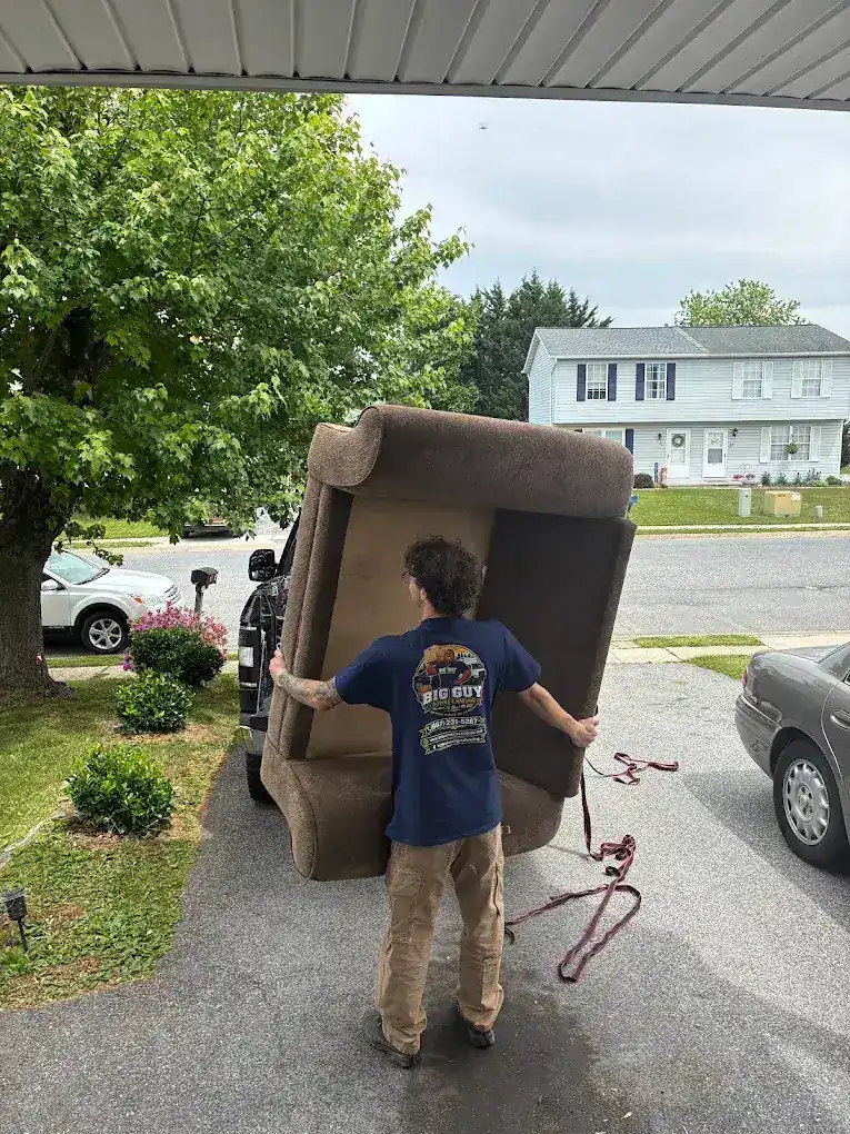 Mover in a Big Guy Moving tee lifting a recliner sofa into a truck